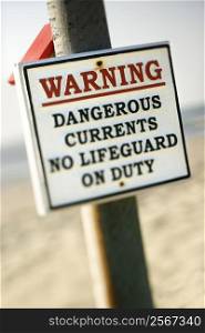 Warning sign on post at the beach with ocean in background.