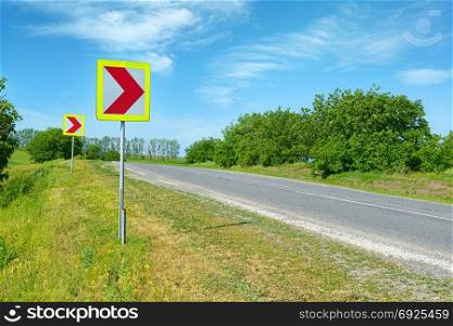 Warning signs for dangerous turn on country road.