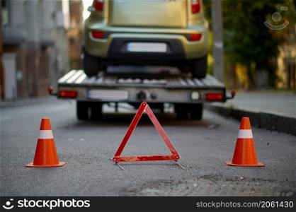 Warning triangle and traffic cone on road. Tow truck towing broken car on highway. Selective focus. Warning triangle and traffic cone on road