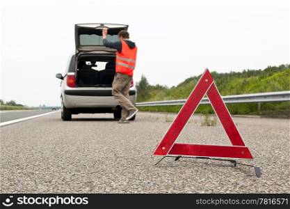 Warning triangle behind a broken down car with the bonnet open on the emergency lane of a highway