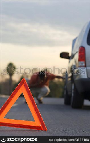 Warning triangle in front of broken down car, man in background