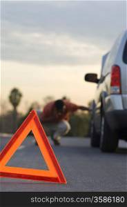 Warning triangle in front of broken down car, man in background