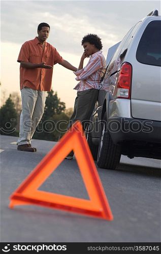 Warning triangle in front of broken down car, people in background