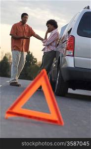 Warning triangle in front of broken down car, people in background