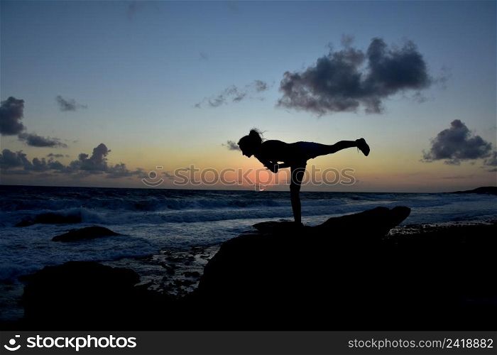 Warrior 3 balance pose along the coast silhouetted at sunrise.