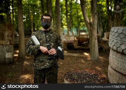 Warrior in camouflage and mask holds paintball gun. Extreme sport with pneumatic weapon and paint bullets or markers, military game outdoors. Warrior in camouflage and mask holds paintball gun