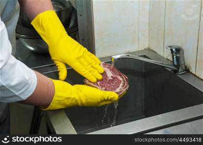 washing and cleaning meat. Hands in gloves washing and cleaning meat at the kitchen sink