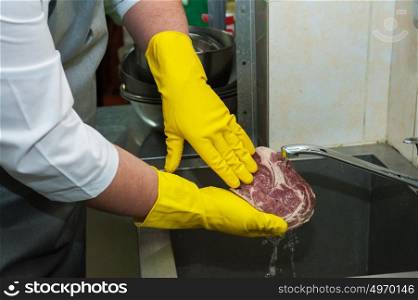 washing and cleaning meat. Hands in gloves washing and cleaning meat at the kitchen sink