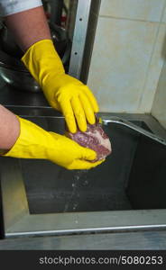 washing and cleaning meat. Hands in gloves washing and cleaning meat at the kitchen sink