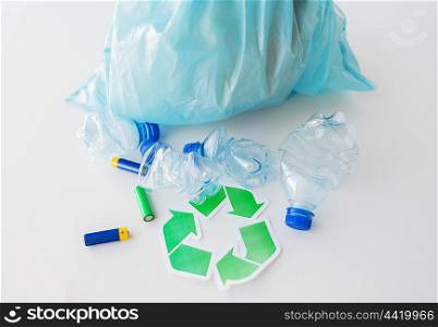 waste recycling, reuse, garbage disposal, environment and ecology concept - close up of used crashed plastic water bottles and batteries with rubbish bag and green recycle symbol