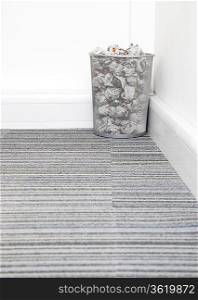 Wastebasket full of crumpled paper in corner on carpet floor in room
