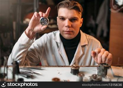 Watch maker holding wrist watch in hand. Watchmaking tools on the table