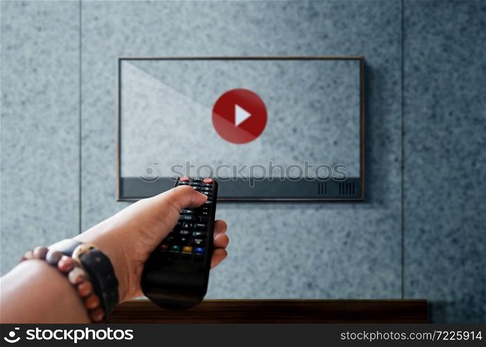 Watching Television Concept. Hand holding TV&rsquo;s Remote Control Playing Youtube Media. Relaxation in Modern Living Room. Focus on Remote