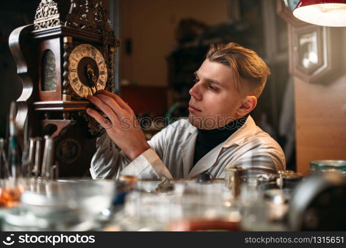 Watchmaker adjusts the mechanism of old wall clock in the workshop.