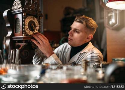 Watchmaker adjusts the mechanism of old wall clock in the workshop.