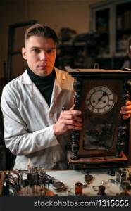 Watchmaker adjusts the mechanism of old wall clock in the workshop.. Watchmaker adjusts the mechanism of old wall clock