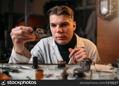 Watchmaker holding with tweezers a gear of old hours. Broken mechanical watches repairing. Watchmaker holding with tweezers a gear of hours