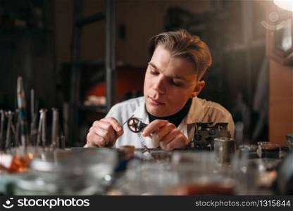 Watchmaker holding with tweezers a gear of old hours. Broken mechanical watches repairing. Watchmaker holding with tweezers a gear of hours