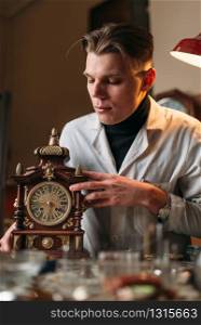 Watchmaker with old mechanical desk clock. Hour workshop