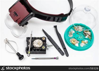 watchmaker workshop - above view of kit of tools with head-mounted magnifier and spare parts for repairing mechanical watch on white background