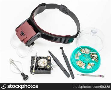 watchmaker workshop - above view of various tools with head-mounted magnifier and spare parts for repairing mechanical watch on white background