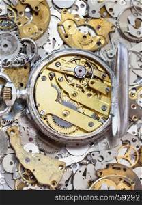 watchmaker workshop - open old silver pocket watch with brass clockwork on pile of clock spare parts