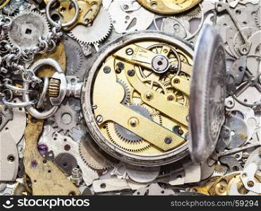 watchmaker workshop - open old silver pocket watch with brass clockwork on heap of clock spare parts