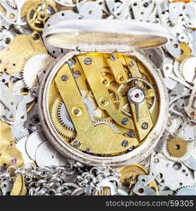 watchmaker workshop - open retro silver pocket watch with brass clockwork on pile of clock spare parts