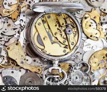 watchmaker workshop - open used silver pocket watch with brass clockwork on pile of clock spare parts