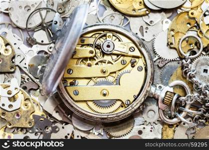 watchmaker workshop - open vintage silver pocket watch with brass clockwork on heap of clock spare parts