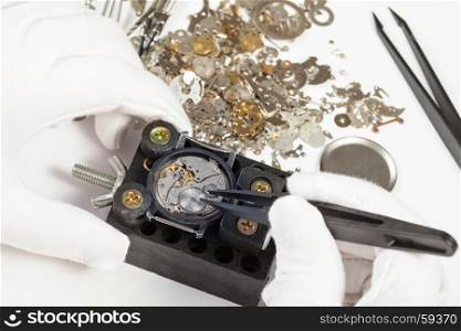 watchmaker workshop - repairing of mechanical wristwatch by tweezers with spare parts on white background