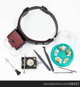 watchmaker workshop - top view of set of tools with head-mounted magnifier and spare parts for repairing mechanical watch on white background