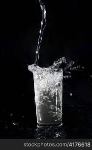 Water being poured in a transparent glass on the black background