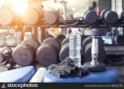 Water bottle in fitness gym with blurred dumbbells background.