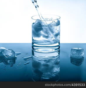 Water cold drink pouring into glass over bright background. Blue colored picture