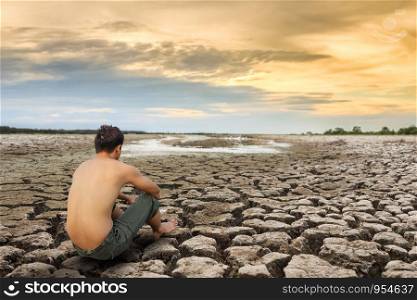 Water crisis, man sit on cracked earth near drying water.