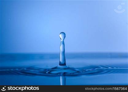 Water drop splash into crystal clear blue water making ripples background. Drop of clear water