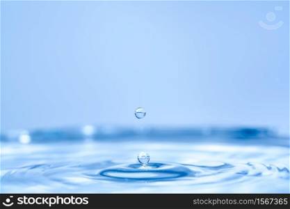 Water drop splash into crystal clear blue water making ripples background. Drop of clear water