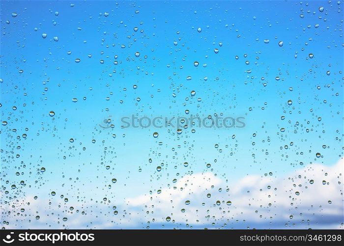 Water droplets on glass against the blue sky with clouds
