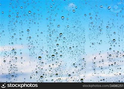 Water droplets on glass against the blue sky with clouds