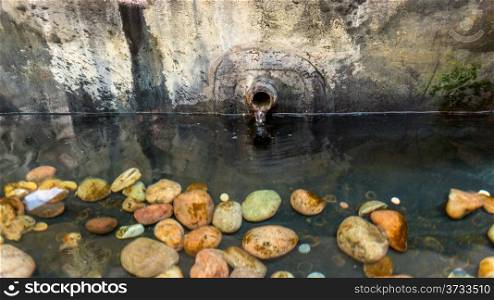 Water flowing out of an old rusted pipe in a pond