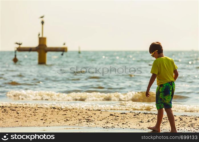 Water fun and joy outside. Little boy walking through the sea ocean. Lonely kid playing outdoors in summer clothes.. Boy walking on beach.