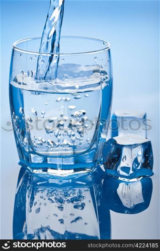 water splashing into glass with ice cubes
