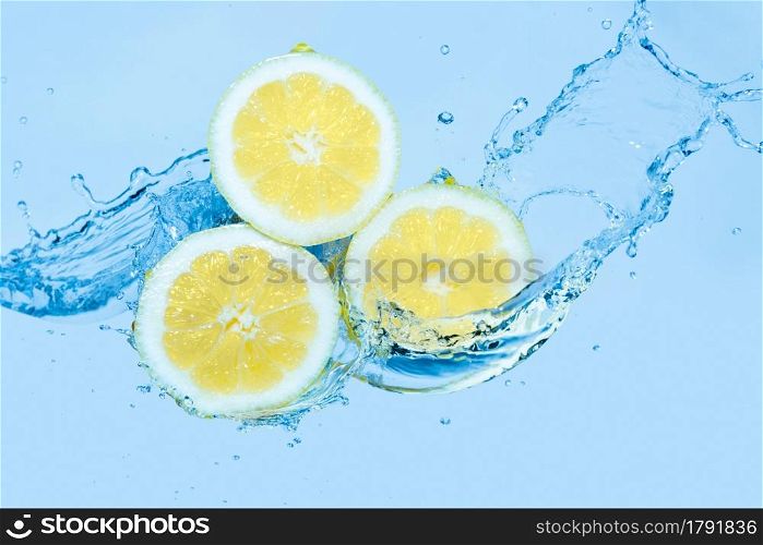 Water splashing on slices of lemon against a light blue background