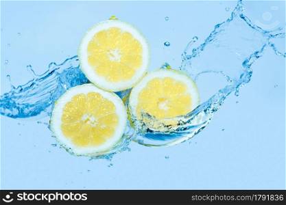Water splashing on slices of lemon against a light blue background