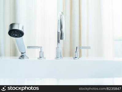 Water tap on white bathtub at window, close up