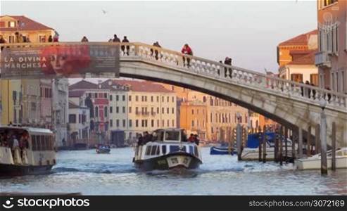 Water trams and motor boats sailing along the Grand Canal under Scalzi Bridge with people walking across it