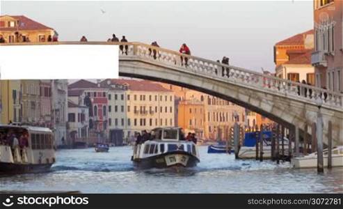 Water trams and motor boats sailing along the Grand Canal under Scalzi Bridge with people walking across it