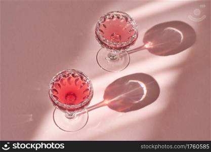 Water with black elder syrup in two glasses on pink background