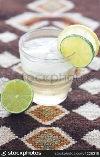 water with lemon and lime in a glass with ice on ethnic mat